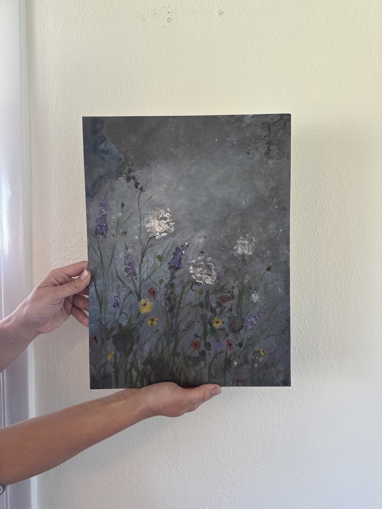 Wildflowers — purple spikes and white umbels rising through a soft grey field, held against a pale wall