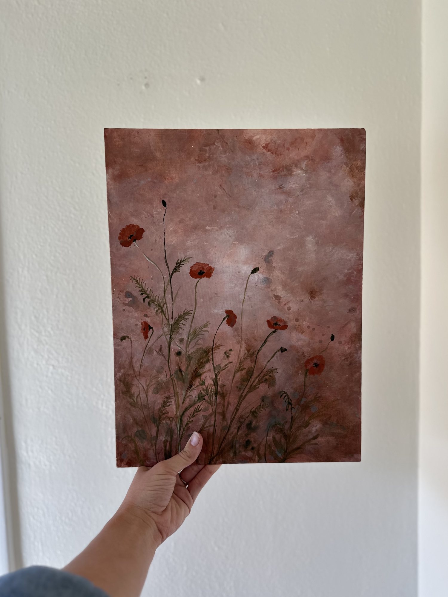 Poppies — red poppies on slender green stems against a dusty rose ground, held against a pale wall