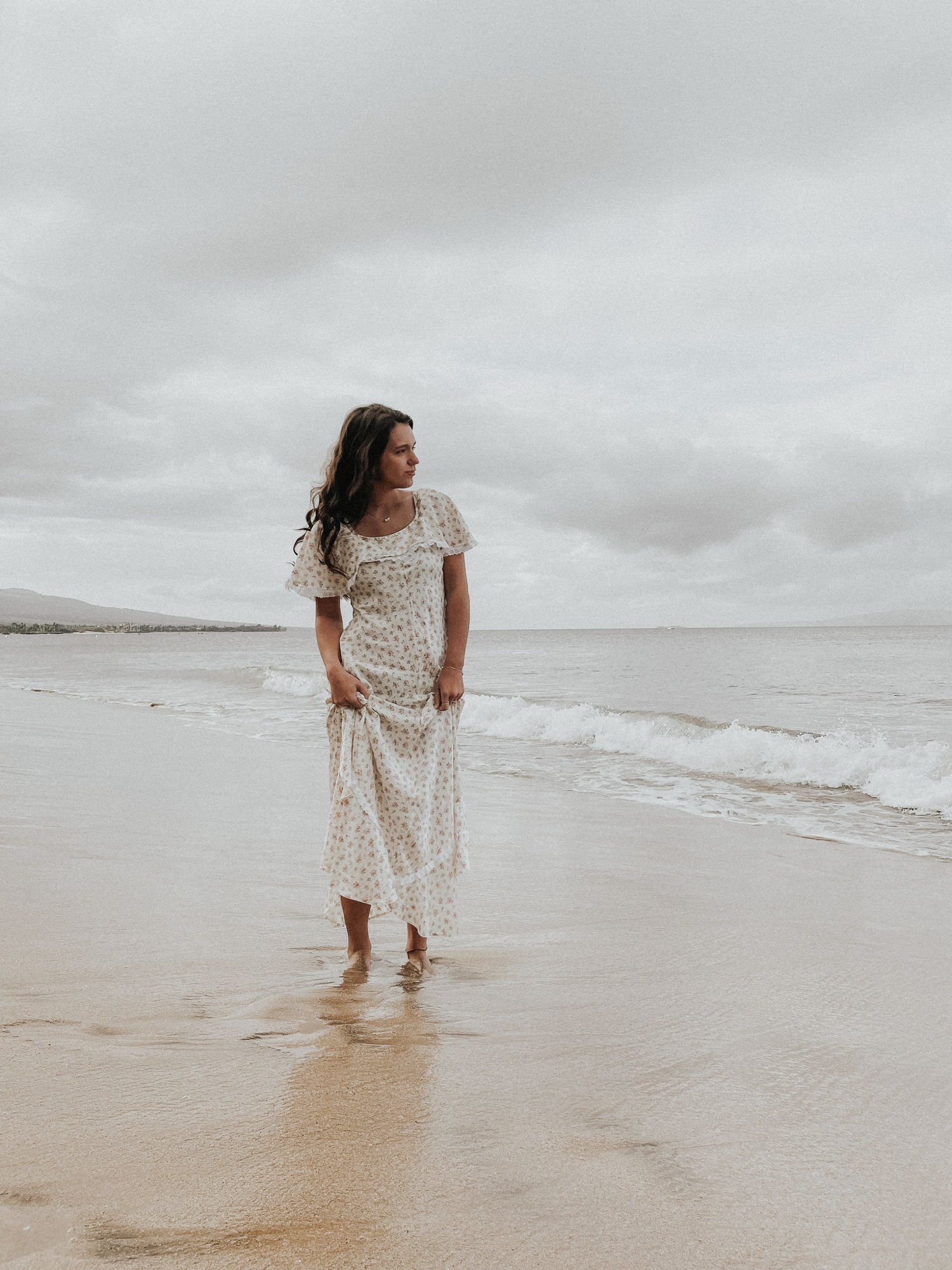 Vivian Soderberg standing barefoot at the edge of the surf on an overcast beach, pale sky and wet sand