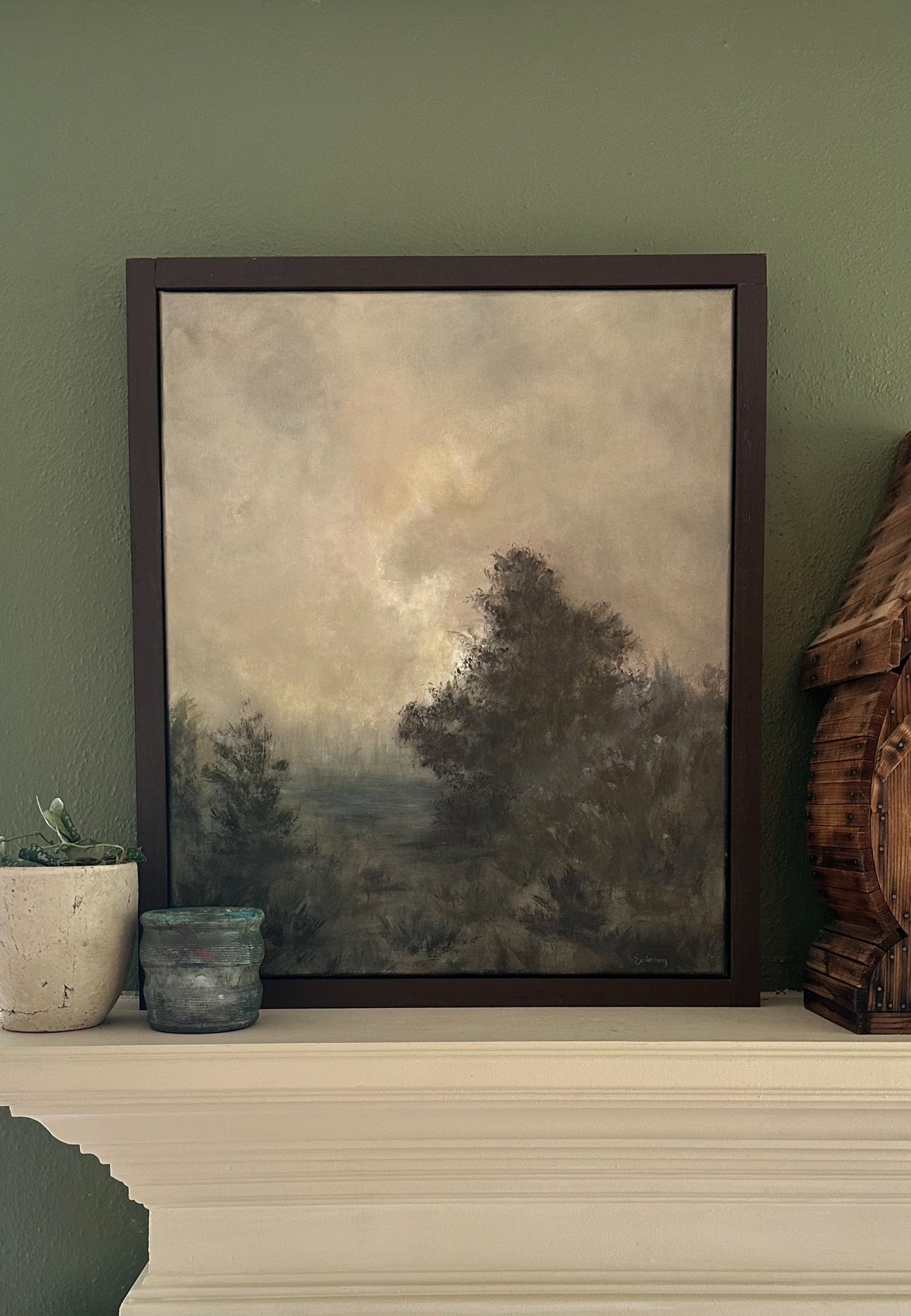 The Valley Over framed on a mantel against a sage-green wall, beside a plant and a pot
